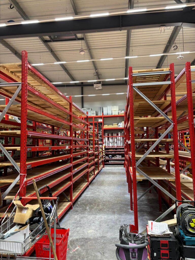 Allée centrale encadrée par des rayonnages métalliques rouges avec plateaux en bois