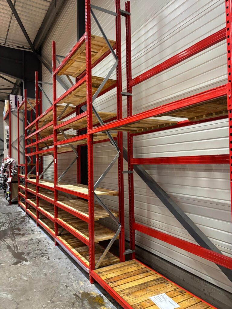 Structure de rayonnage rouge équipée de plateaux en bois contre un mur du magasin